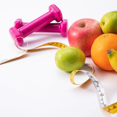 A fitness composition with pink dumbbells, fresh fruits, and measuring tape on a white background